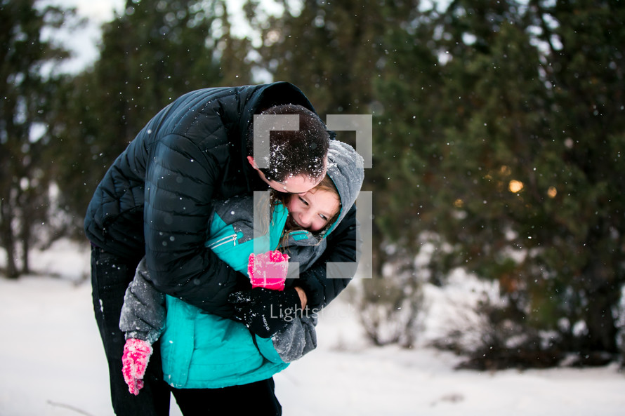 a father hugging a girl child in a winter coat standing outdoors in snow 