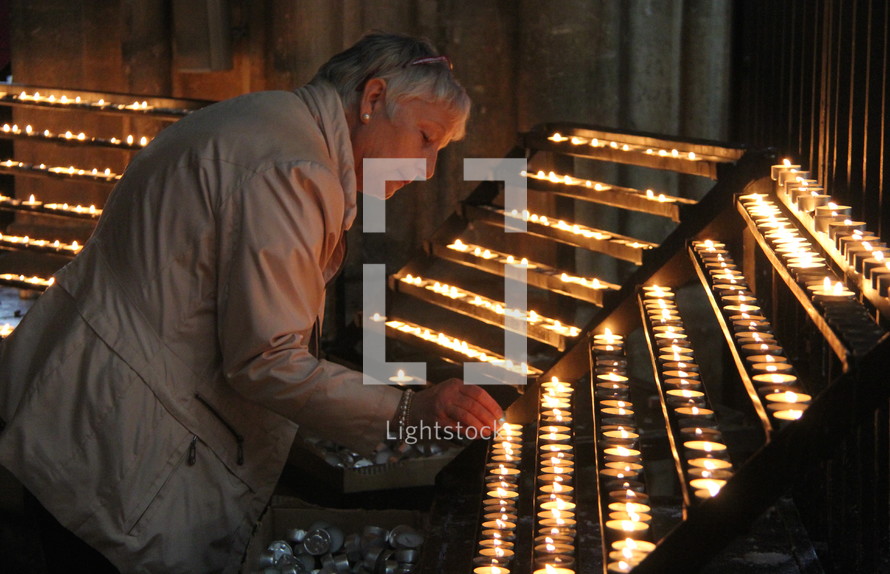 Lady lighting a votive or prayer candle in the Catholic Cathedral.