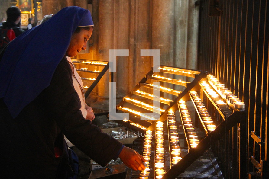 Nun lighting votive or prayer candle in Catholic Cathedral.