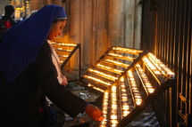 Nun lighting votive or prayer candle in Catholic Cathedral.