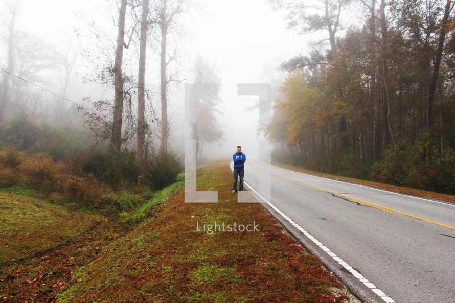 a man standing on the side of a foggy road 