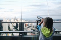 a girl looking through a telescope on the rooftop of a building in a city 
