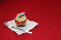 Cupcake decorated with cream cheese, sprinkles and a fondant rainbow 