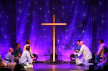 performers on stage kneeling before a cross