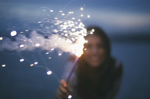 A woman holding a fiery sparkler.
