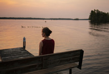 a woman sitting alone at the edge of a pond thinking and praying 