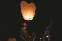 man releasing a heart shaped paper lantern at night 