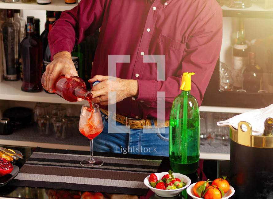 Man expertly preparing a colorful drink at a stylish bar setting