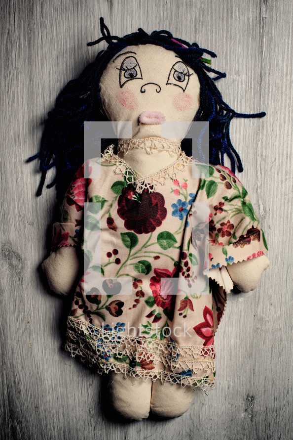 Handmade rag doll with button eyes and yarn hair is lying on a wooden background