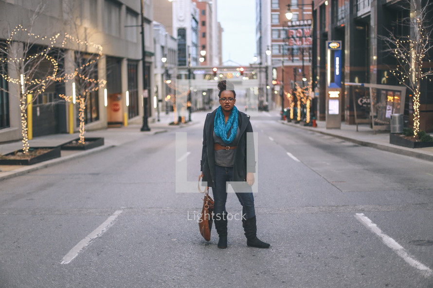 woman standing in the middle of a street dragging her purse 