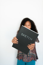 teen girl holding out a sketch book 