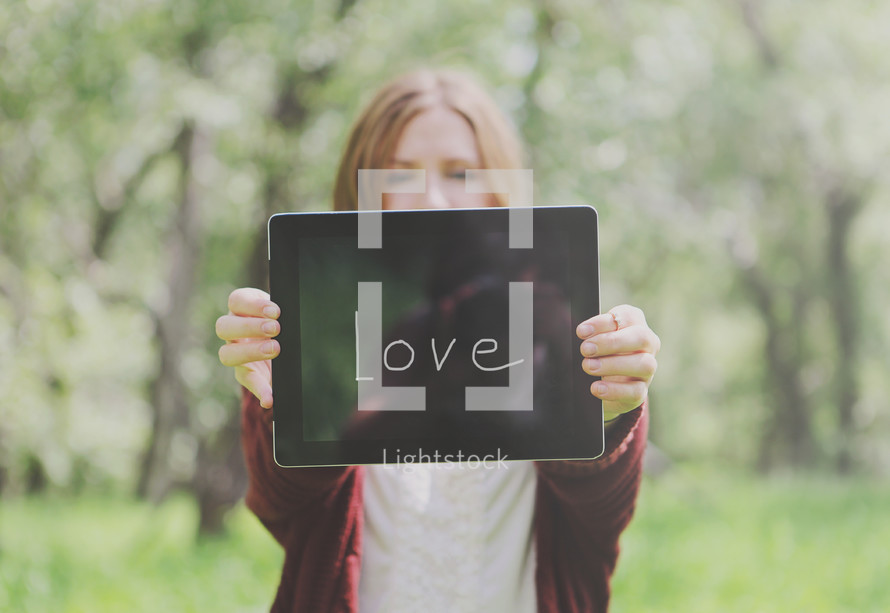 Young woman holding out a tablet that says, "Love."