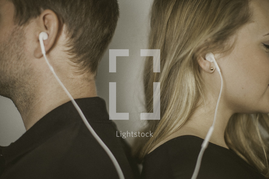 couple standing back to back listening to earbuds 