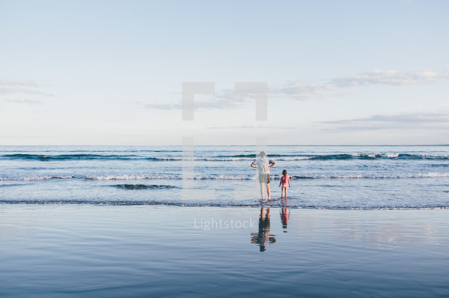 father and daughter standing in the water at a beach 