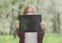 Young woman outdoors holding up blank tablet - space for text