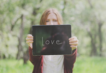 Young woman holding out a tablet that says, "Love."