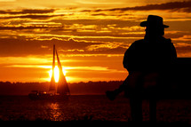 man watches sailboat at sunset 