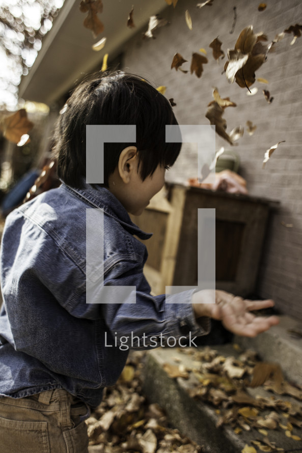 child throwing fall leaves