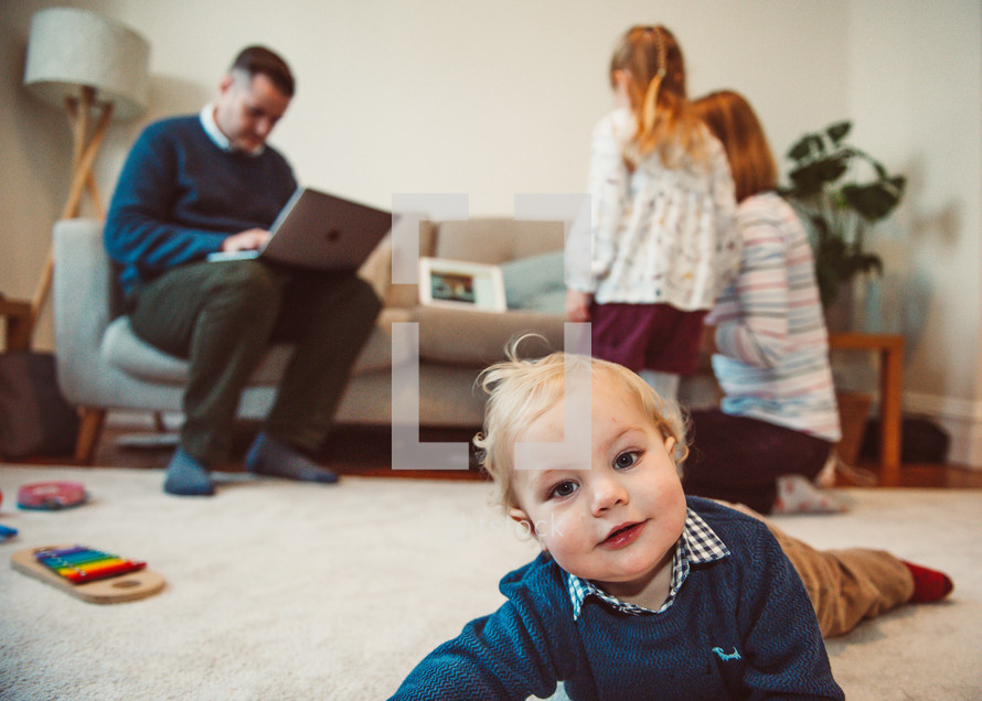 toddler boy crawling on the floor as a family logs in on a computer for an online worship service 