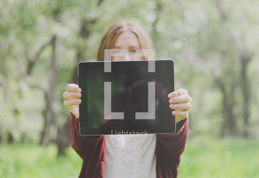 Young woman outdoors holding up blank tablet - space for text