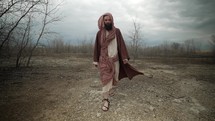 Jesus Christ dressed in brown robes and shroud walking alone in cinematic, slow motion in the wilderness temptation by the Devil or Satan for 40 days and 40 nights fasting and praying. Could also be used to depict a biblical prophet like Noah, Abraham, Elijah, Moses or John the baptist. 