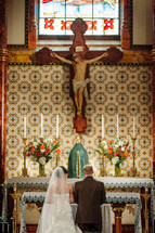 crucifix above a kneeling bride and groom 