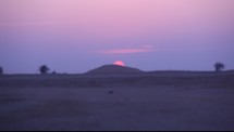 sun setting behind a hill in a desert 