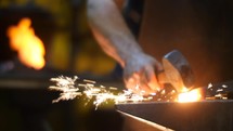 Blacksmith hit with Hammer Hot Metal with Sparks in a Workshop Behind a Forge