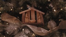 Wooden nativity ornament on a Christmas tree with gold ribbon and lights