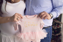 mother and father holding up an infant onesie with a tutu 