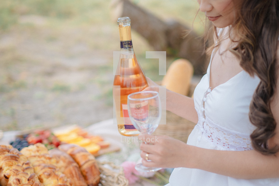 a woman pouring a bottle of wine at a picnic 