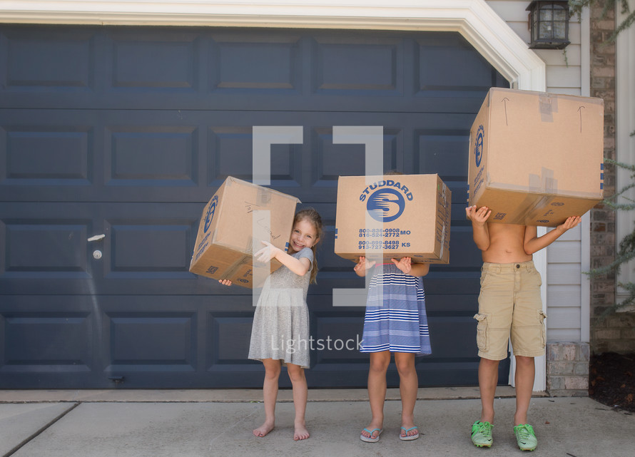 children holding moving boxes in front of a garage 