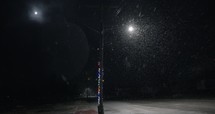 Slow motion snow at night in front of city street light, Snowflakes falling in slow motion during winter snow storm at nighttime.