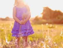 a child holding flowers in a field at sunset 