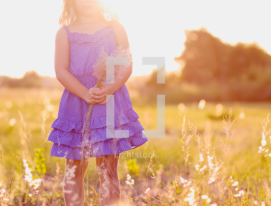 a child holding flowers in a field at sunset 