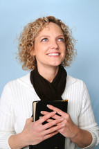 Woman smiling, holding a bible, looking up 