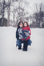 mother and daughter in the snow holding a stuffed animal elephant 