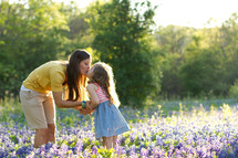 Mother and young daughter kissing in field of purple wildflowers