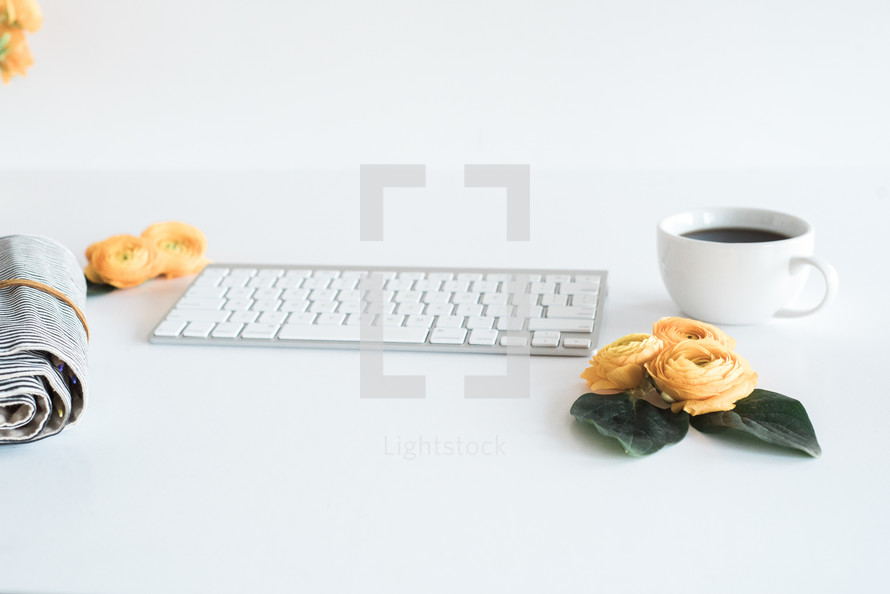 computer keyboard, yellow roses, pencil case, coffee mug on a desk 