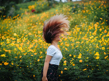 a woman flipping her hair in a field of yellow flowers 