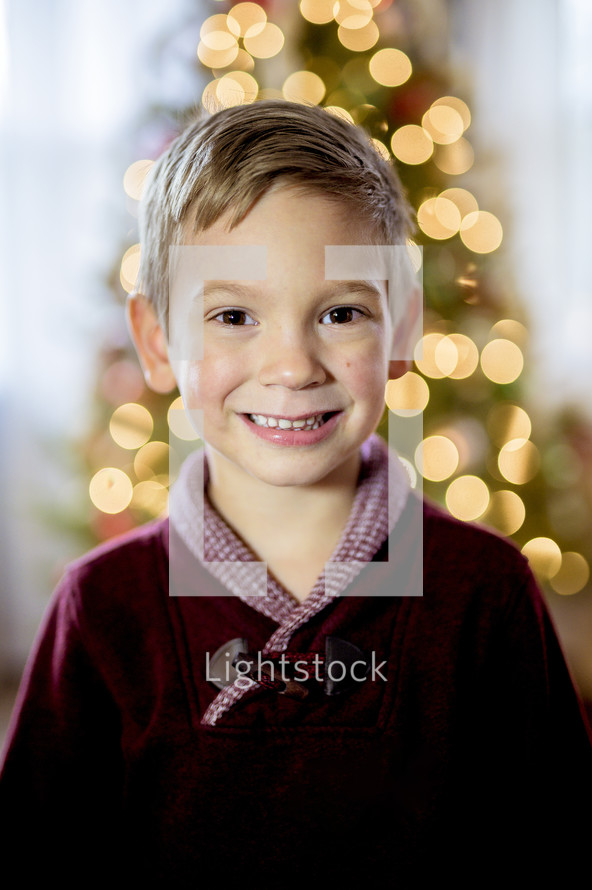 smiling boy standing in front of a Christmas tree 
