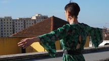 Woman lifting up her arms in a dress on a rooftop.