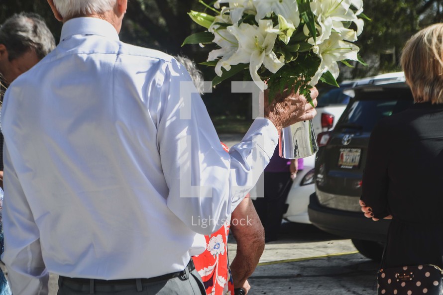 elderly man carrying a vase of flowers 