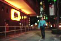 blurry image of a man on a city sidewalk at night 