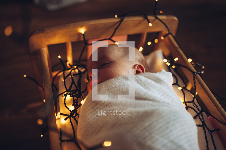 swaddled baby surrounded by Christmas lights 