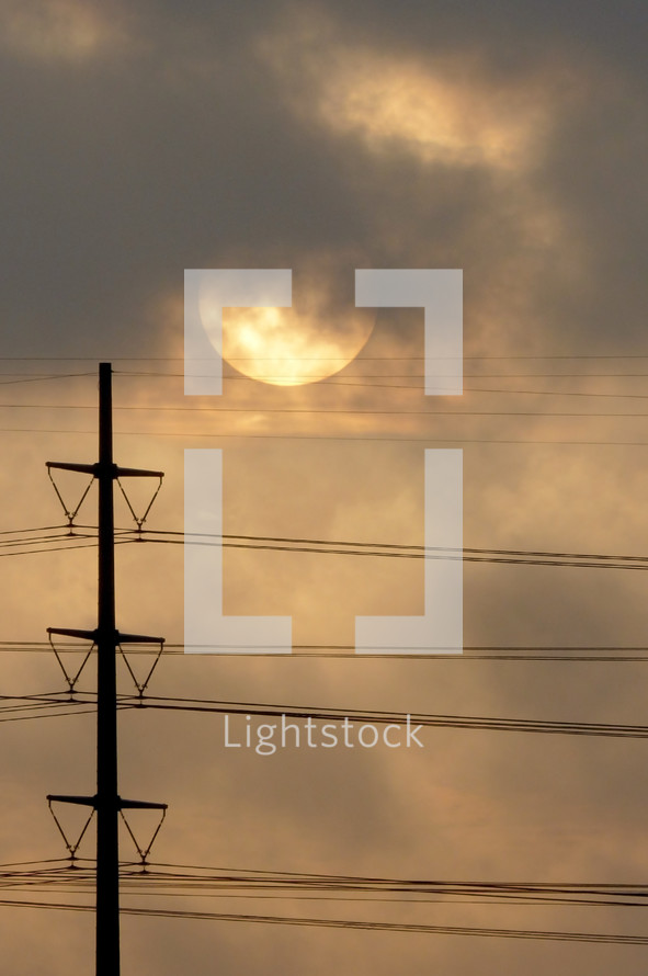 power lines, the sun, and clouds in the sky 