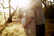 husband with his arms around his pregnant wife glowing in the sunlight