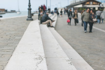 People sitting and walking on a long paved pier.