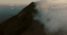 Tilt-up aerial of Fuego volcano covered by clouds during sunset in Guatemala	