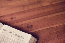 A Bible open to the Song of Solomon on a wooden table.